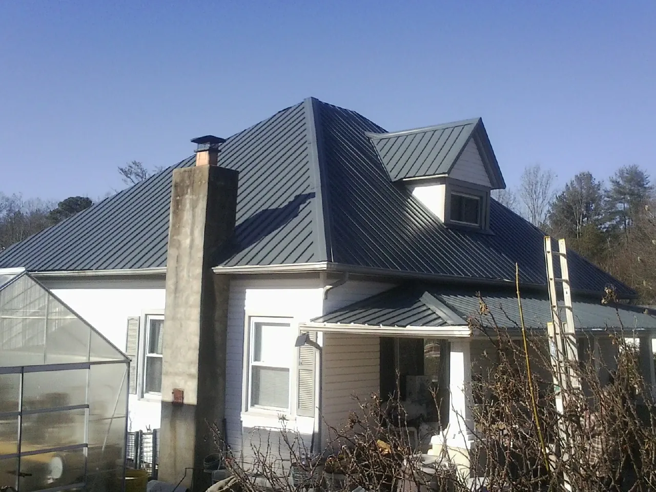 Dark blue standing seam metal roof on a white farmhouse with dormer — Slate & Tile Roof Repair by Roofing Brothers in Augusta Springs