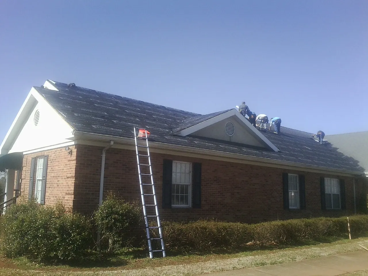 Crew tearing shingles off a brick ranch roof with a ladder set — Emergency Roof Repair work by our crew in Augusta Springs