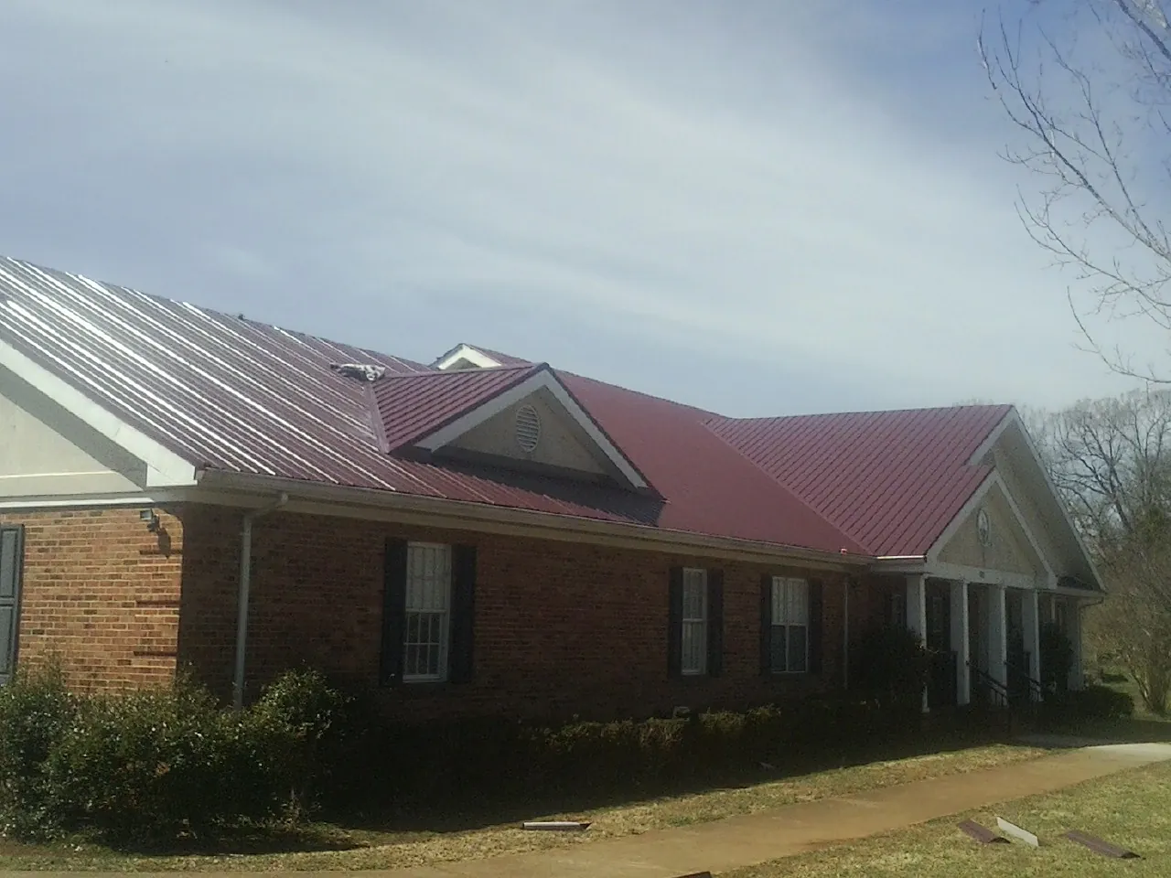 Red metal roof with gabled entries on a long brick building, from a Hail Damage Roof Repair job in Augusta Springs