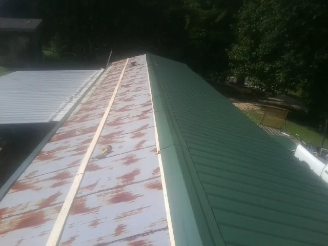 Old rusted panels beside newly installed green metal roofing — Wind Damage Roof Repair by Roofing Brothers in Augusta Springs