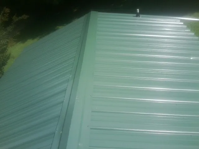 New green metal panels meeting at the ridge of a roof — Flat Roof Repair work by our crew in Augusta Springs