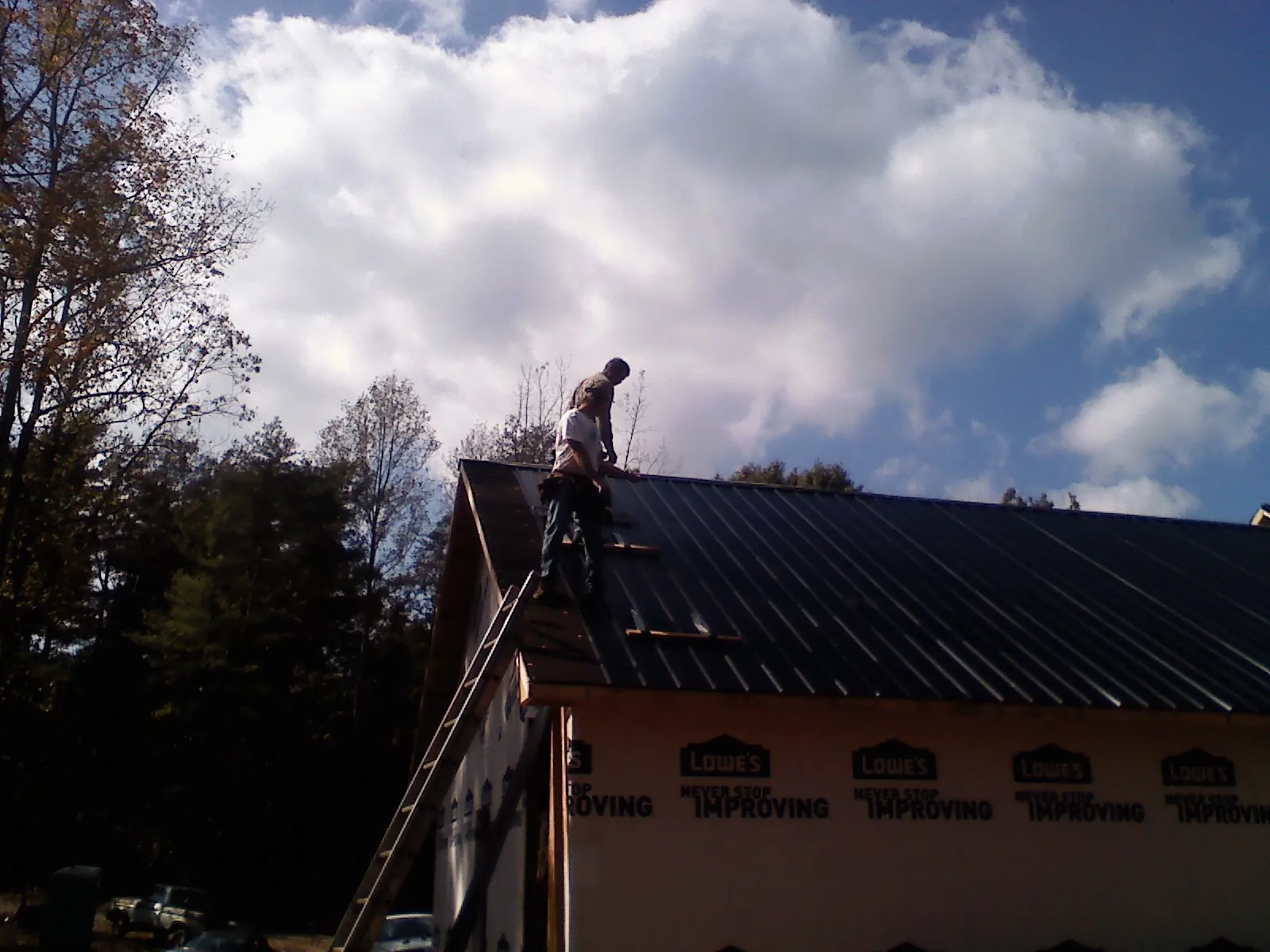 Roofer fastening dark metal panels high against a cloudy sky, from a Roof Inspection job in Augusta Springs