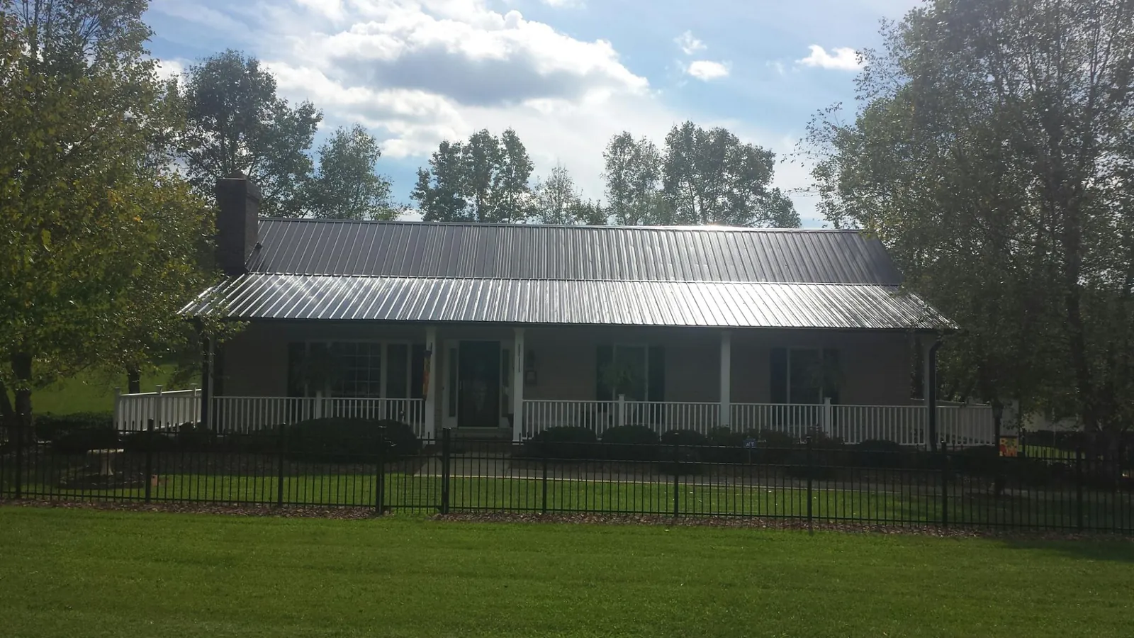 Gray metal roof on a brick ranch with a full width front porch — Gutter Guard Installation work by our crew in Augusta Springs