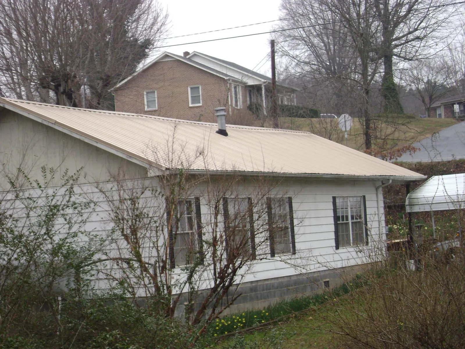 Tan metal roof on a white sided house set into a hillside — Commercial Roofing by Roofing Brothers in Augusta Springs